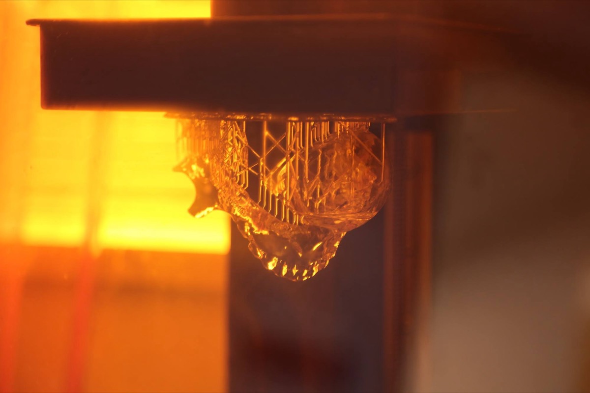 A resin model lifting out of the tank of a stereolithography 3D printer under amber light